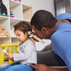 Father using otoscope on child in child's bedroom
